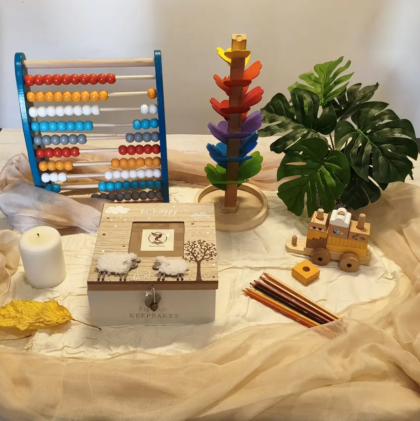 Zona con juguetes montessori, plantas, telas, lápices de colores, velas aromáticas y cajas de madera.